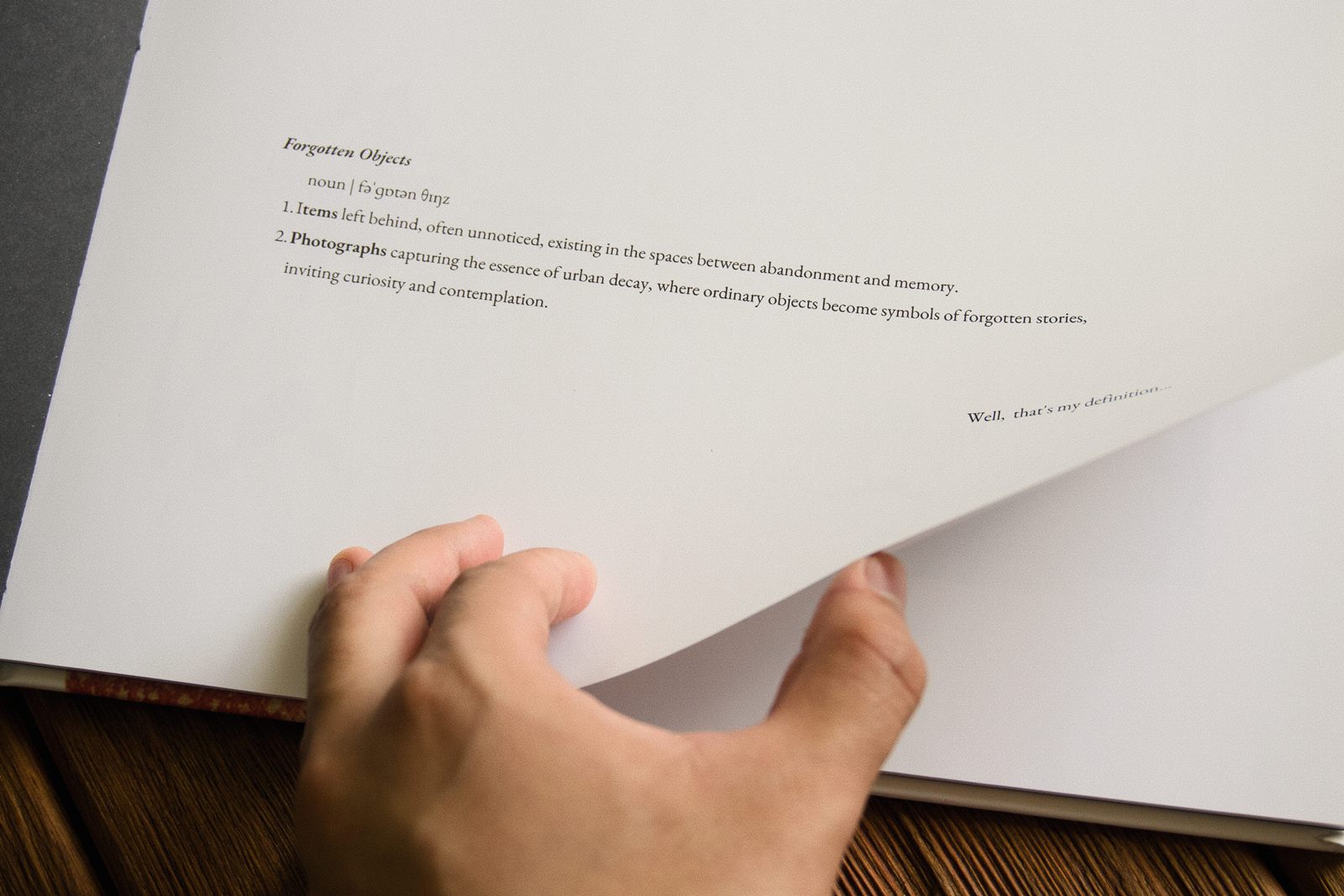 Mano pasando una página del libro impreso Forgotten Things, con la definición «Forgotten Objects» sobre papel blanco