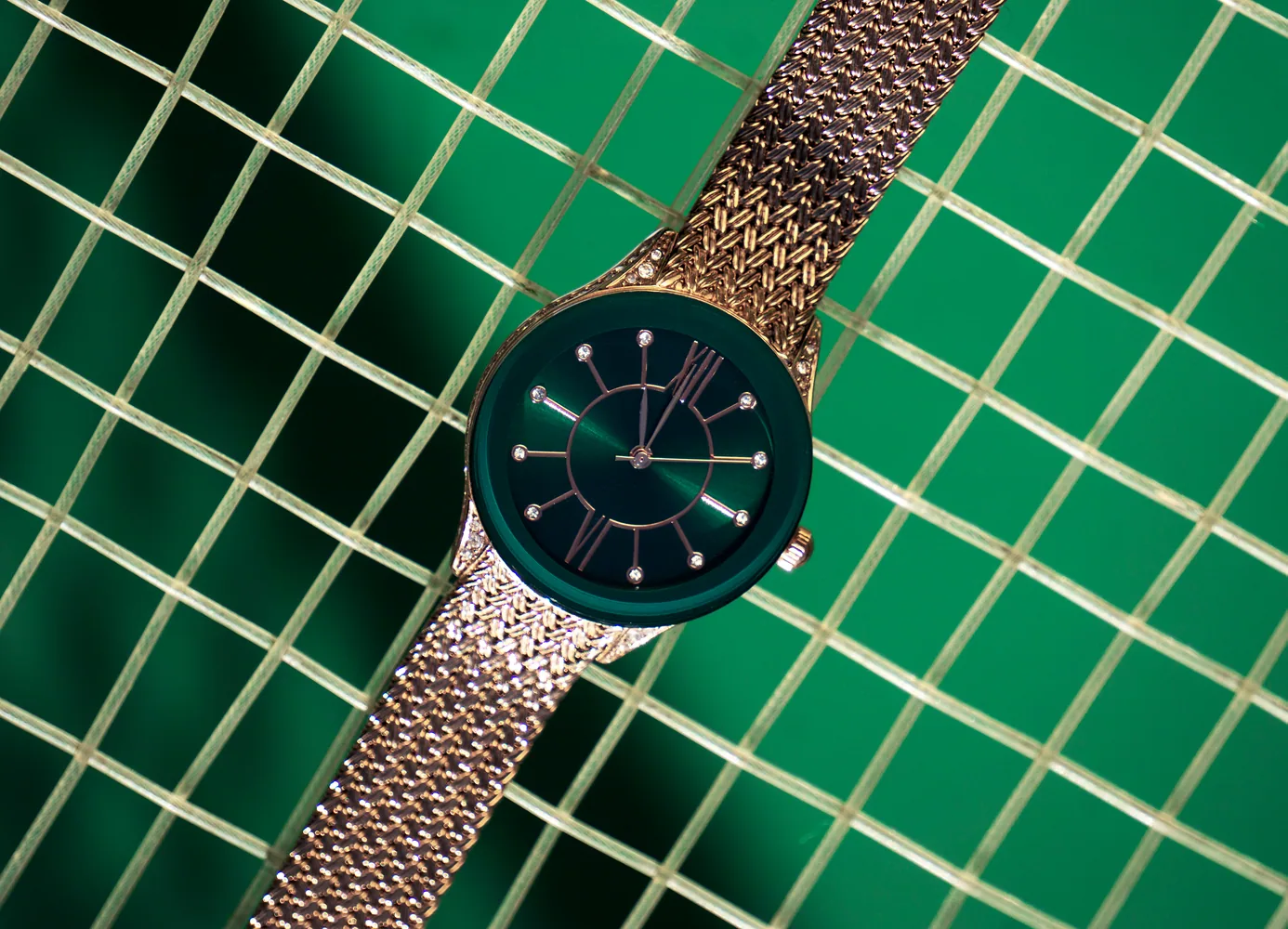 Reloj de brazalete dorado con carátula verde sobre azulejo verde